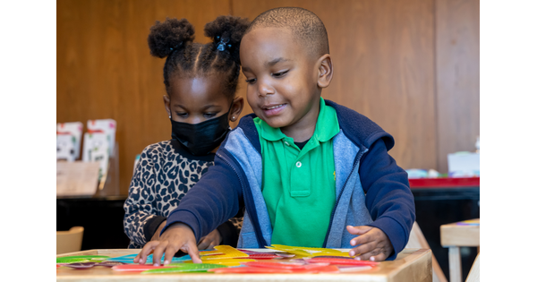 Two small children play with pieces of paper at a table in the Carter&#039;s Family Pop-up Space.