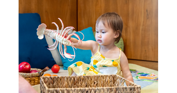 A baby sits on the floor playing with toys from a basket.