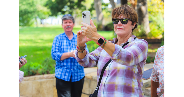 A middle-aged White woman takes a photo of something with her phone.