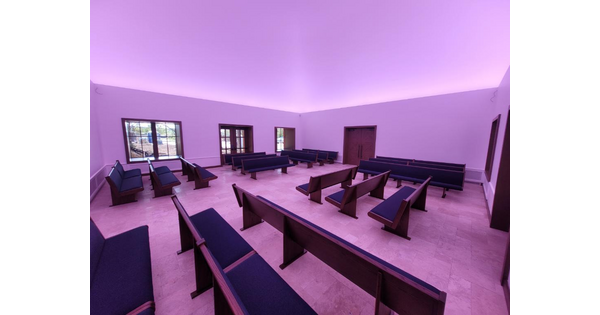 A large room filled with rows of church pews and bathed in a purple light.