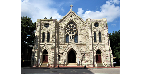 The facade of a stone church with three entrance portals, the center one beneath a stained glass rose window.