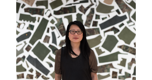 A portrait of an Asian woman with glasses and long black hair standing in front of an art installation.