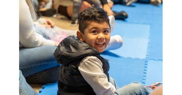A smiling child sits on mats on the floor in a Carter gallery.