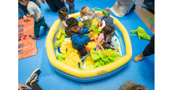 Five small children sit in a baby pool filled with tissue paper and toys in the Carter&#039;s Atrium.