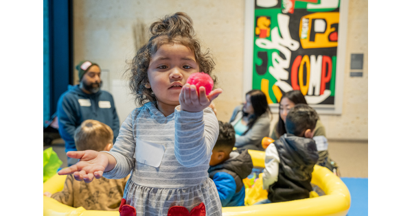 A close-up of a child standing in a Carter gallery holding up a red toy in their hand.