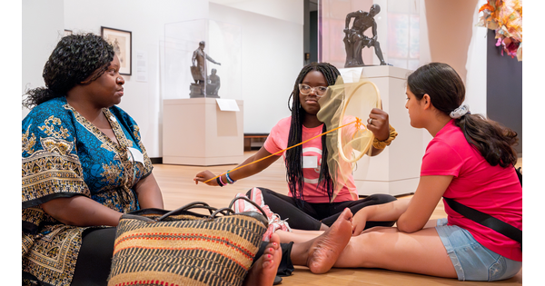 An adult and two teenagers sit on the floor of a Carter gallery making art.