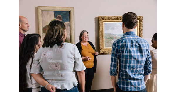A group of adults stand around a Carter educator who gestures toward artwork in a gallery.
