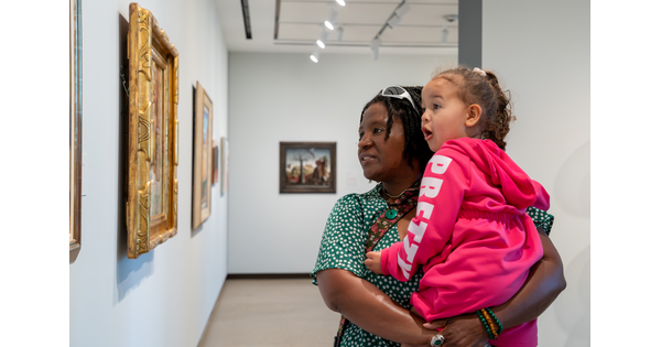 A Black woman holds a child in her arms as they look at artwork in a Carter gallery.
