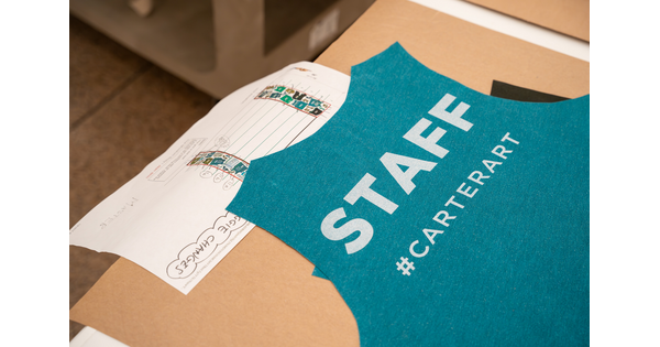 The back of a teal green t-shirt that says &quot;Staff&quot; on a table.