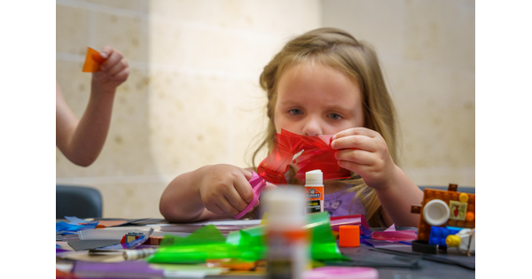 A child cuts red paper at a table in the Carter&#039;s Atrium.