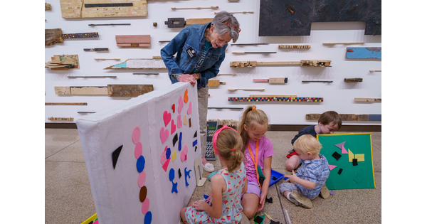 Children sit on the floor of a Carter gallery adding shapes to a felt board held by a Carter educator.