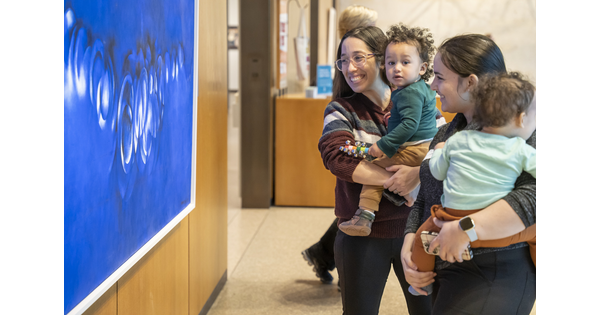 Smiling adults holding babies on their hips look at artwork in a Carter gallery.