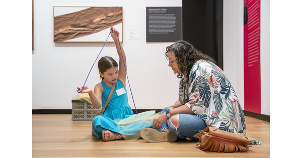 An adult and child sit on the floor of a Carter gallery making artwork with yarn and fabric.