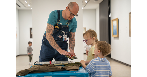 A Carter educator shows two children touchable artwork at a table in a Carter gallery.