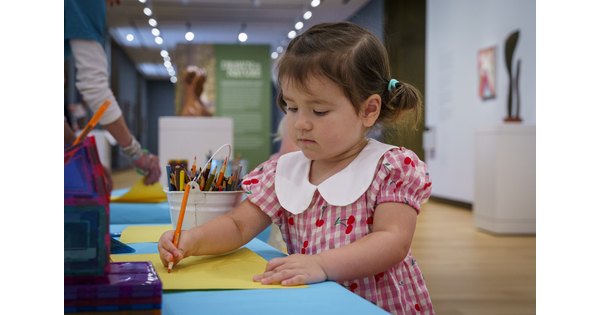 A child draws on a sheet of paper at a table in a Carter gallery.