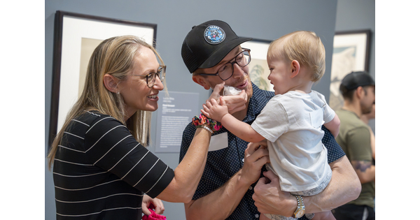 Two adults, one holding a baby, play with props in a Carter gallery.