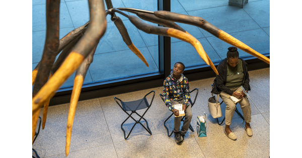 An adult and a child sit on stools in a Carter gallery drawing a sculpture that hangs from the ceiling.