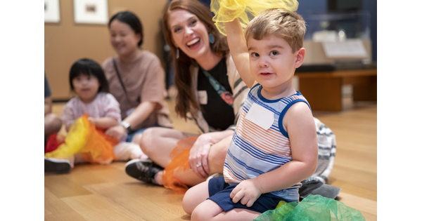 A seated White child waves a piece of colored fabric over his head in a Carter gallery.