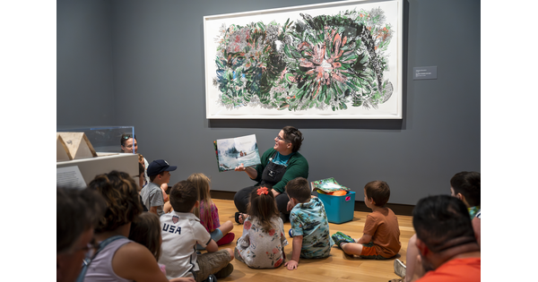 A group of children sit on the floor in a Carter gallery as a Carter educator reads a story.