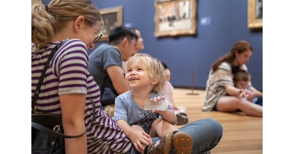 A smiling child sits on an adult&#039;s lap on the floor of a Carter gallery.