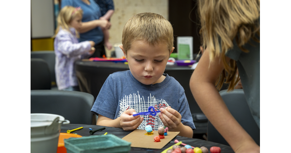 A child stands at a table in the Carter&#039;s Atrium focused on making artwork.