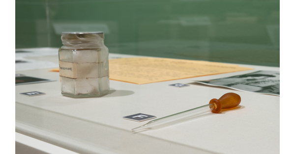 A sealed glass jar sits next to a glass pipette in a display case.