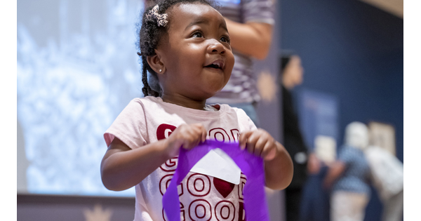 A black child smiles as she holds a purple streamer in a Carter gallery.