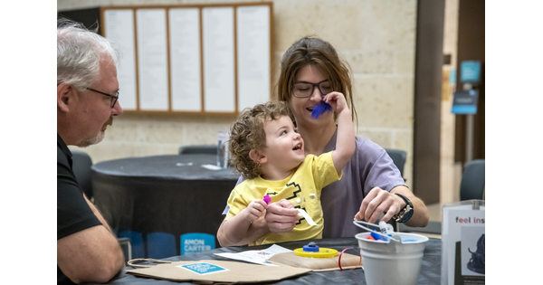 A White child sits on the lap of a woman as they laugh and make art at a table in the Carter's Atrium.