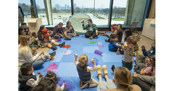 A group of adults and children are seated on the floor of a Carter gallery around an educator.