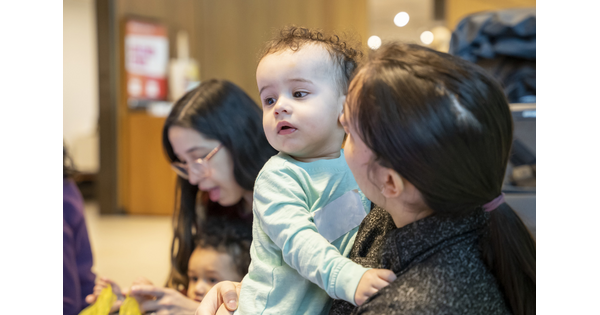 An adult holds a White baby with curly hair as they play in the Carter's Family Pop-up Space.
