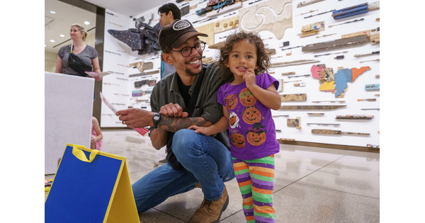 A medium-skinned man squats next to a medium-skinned child participating in an activity in a Carter gallery.
