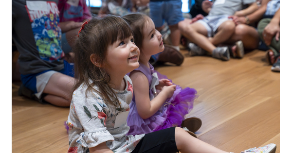 A close-up of two smiling White children sitting on the floor of a Carter gallery.