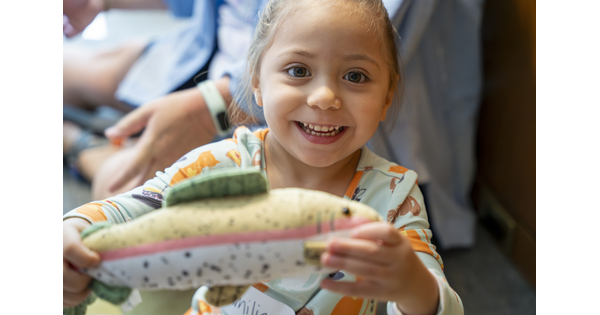 A close-up of a smiling child who is holding up a toy to see.