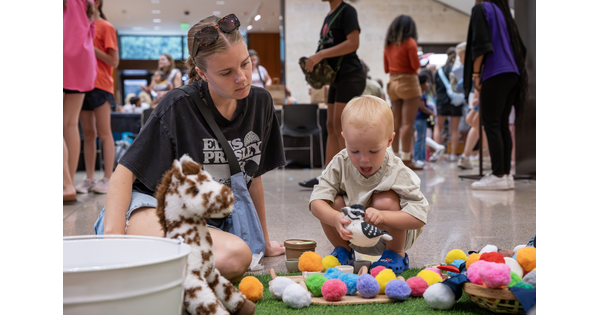 A White woman and small child on the floor of the Carter Atrium playing with colorful pompoms.