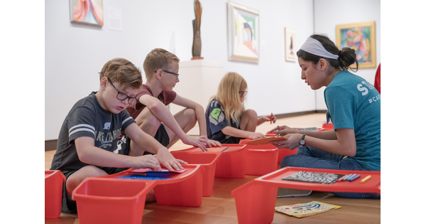 Three middle-school age children and a Carter educator sit on the floor of a gallery making art.