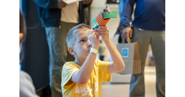 A White child looks in a tube made from colored construction paper in the Carter's Atrium.