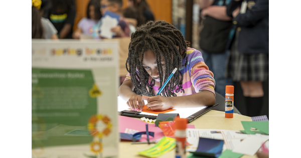 A black tween, focused on making art, leans over a table in the Carter's Library.
