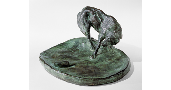 A bronze sculpture of a wolf staring at a bottle on the ground.