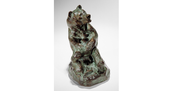 A bronze sculpture of a sitting bear holding a jug in its paws.