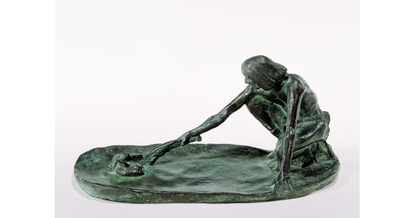 A bronze sculpture of a squatting Indigenous man holding a stick in his outstretched arm toward a snake on the ground.