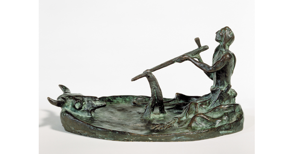 A bronze sculpture of a kneeling Native American man smoking a pipe in front of a bison skull.