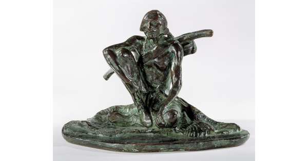 A bronze sculpture with a slight green patina of an Indigenous man seated on the ground.