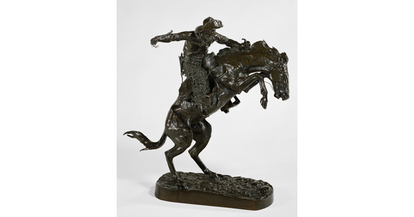 A bronze sculpture of a cowboy balancing on a rearing horse.