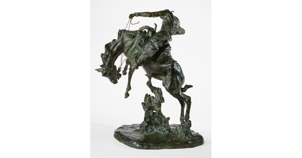 A bronze sculpture of a cowboy on horseback holding the reins as the horse raises up on its hind legs.