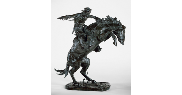 A bronze sculpture of a cowboy balancing on a rearing horse.