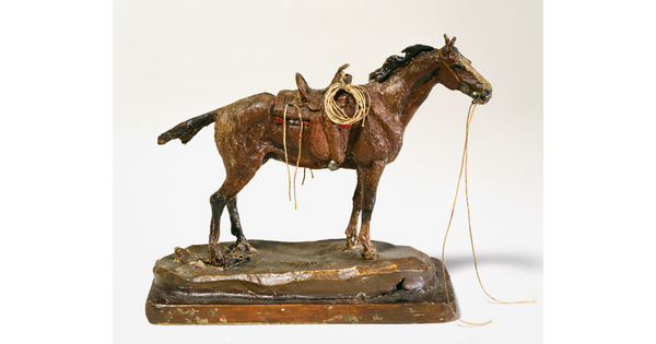 A sculpture of a standing, saddled horse with reins falling from the bridle.