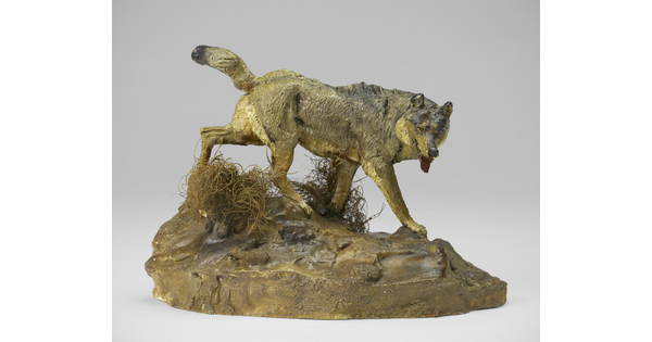 A painted sculpture of a wolf walking across patches of grass on a rock.