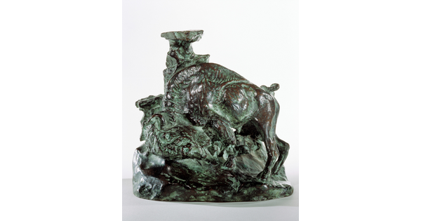 A bronze sculpture of a bison, head bent toward the ground, leaning against what might be a tree trunk to scratch its shoulder.