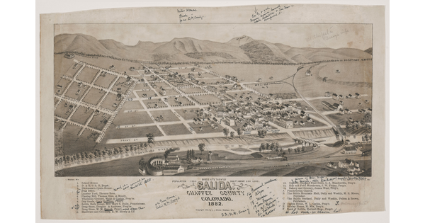 A black-and-white print of a bird's eye view of a town showing the grid of roads on a flat plain with mountains in the distance.