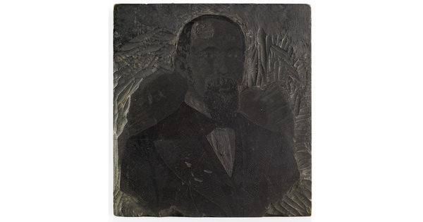 A metal printing block with a portrait of the head and shoulders of a balding man with a goatee wearing a suit.
